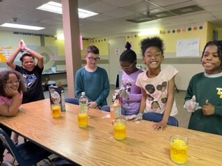 a group of 6 smiling students performing a science experiment