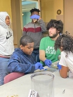 five students gathered around a table doing a science experiment