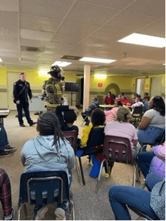 A class of student listening to a fireman dressed in all of his gear talk