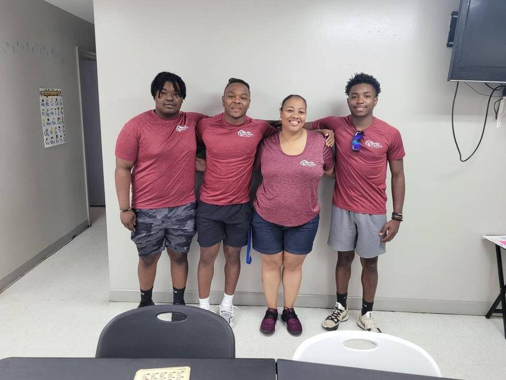 Three boys and a woman posing against a wall and smiling