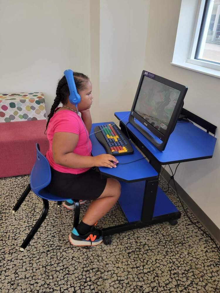 A girl sitting at a computer with blue headphones on