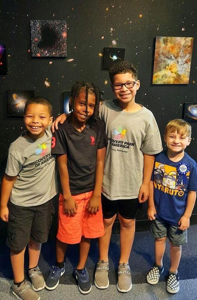 A group of 4 boys smiling with each other and they are standing in front of a picture of space.