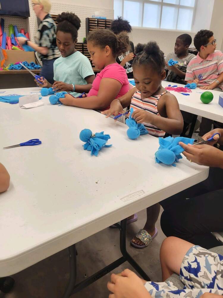 3 girls sitting at a table while cutting fabric in the shape of an octopus.