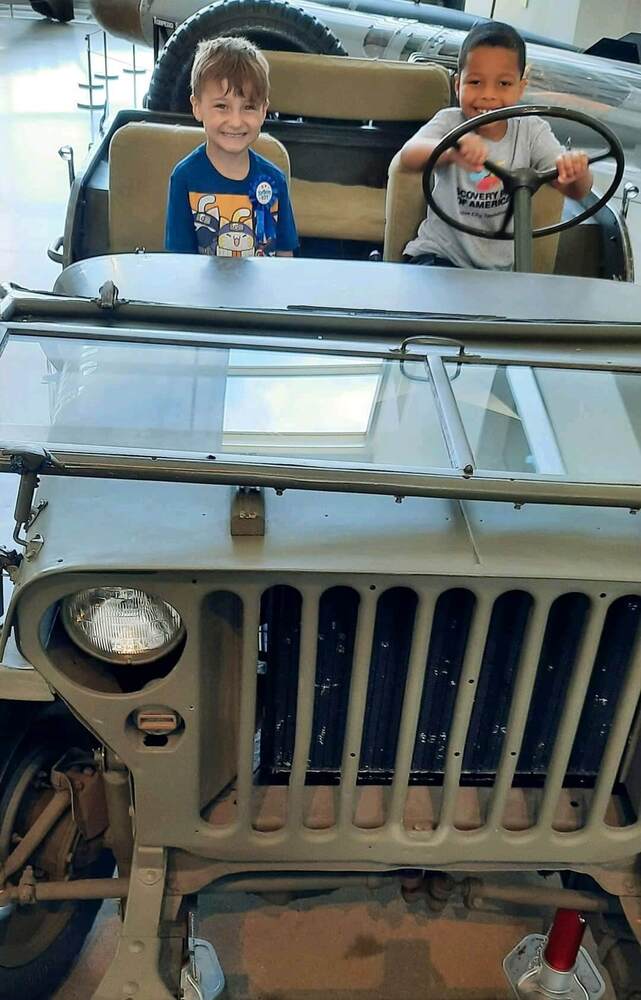 Two young boys pretending to drive an old car.