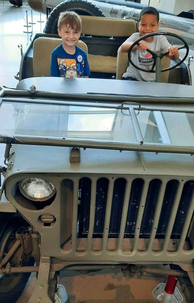 Two young boys pretending to drive an old car.