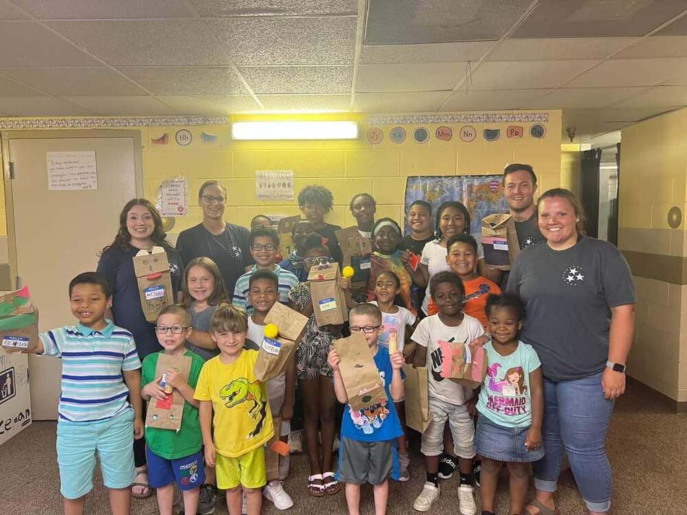 A group of MEA students and teacher holding up their brown paper bag puppets.