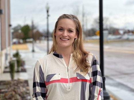 Allicia Austin stops on a sidewalk outside and smiles brightly.