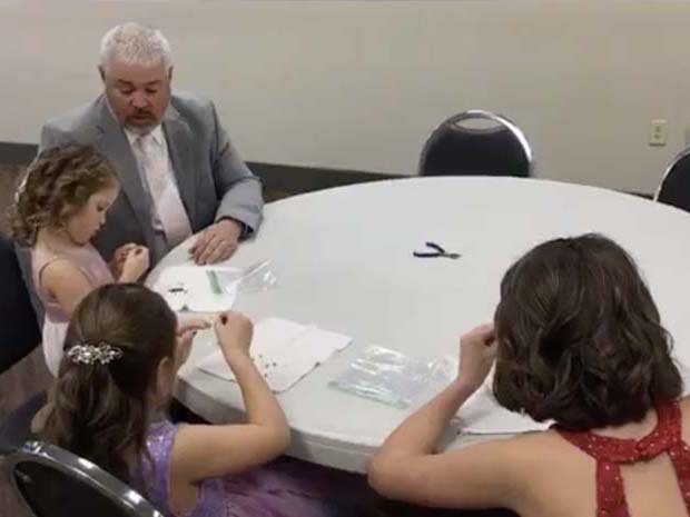 A father sits with his 3 daughters and helps them complete crafts.