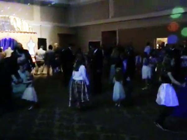 Dads are dancing on a dark dance floor with lots of flashing lights with their daughters.