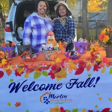 Two women dressed as scarecrows stand behind a welcoming table with buckets of candy.