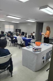 A woman stands next to a WCP table while talking to a group of elderly people.