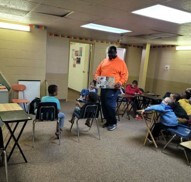 A man walking around with a book reading to children in a classroom.