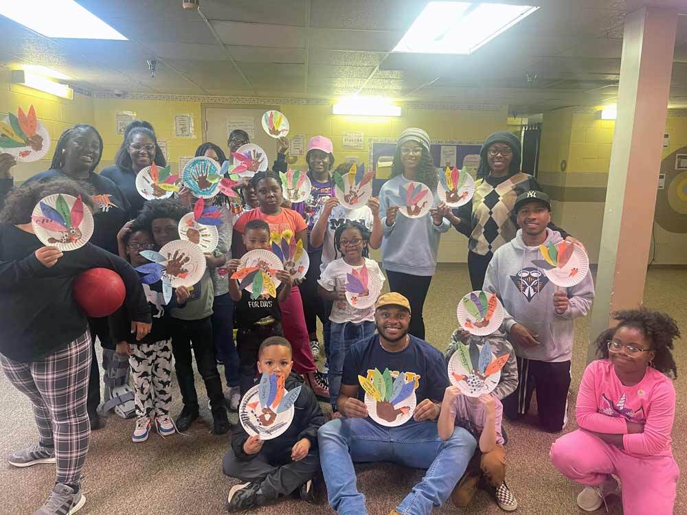 A large group of of MEA kids with UT Martin volunteers all proudly hold up their paper plate turkeys.