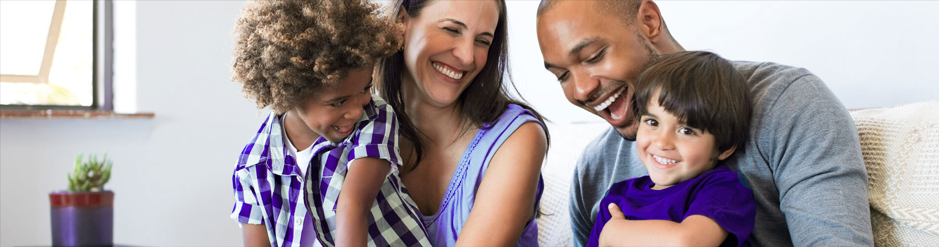 A young family laughing together while sitting on a couch.